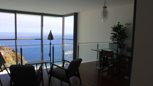 A spacious room with a large window overlooking the sea, a dining area with a table and chairs, and a potted plant. - Sea House Madeira - Atlantic Ocean (garajau)