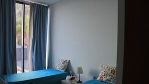 A room with two beds, each with a blue bedspread, a bedside table with a lamp, and floral-patterned pillows. - Sea House Madeira - Atlantic Ocean (garajau)