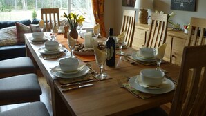A dining room with a long table set for a meal, featuring white plates, glasses, and cutlery. - Fabulous location, luxury lodge for 8+2 in cots, hot tub, garden, garage, dogs   (Aviemore)