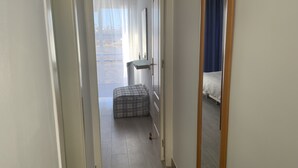 A narrow hallway with a checkered ottoman, a bed with a blue curtain, and a view of the outdoors through a window with sheer curtains. - Fantastic Views Amadores, Wifi (Mogán)