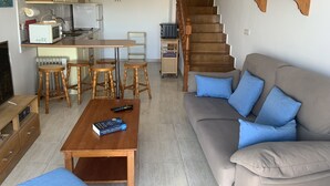 A living room with a sofa, a coffee table, and a kitchen area with a dining table and stools. - Fantastic Views Amadores, Wifi (Mogán)