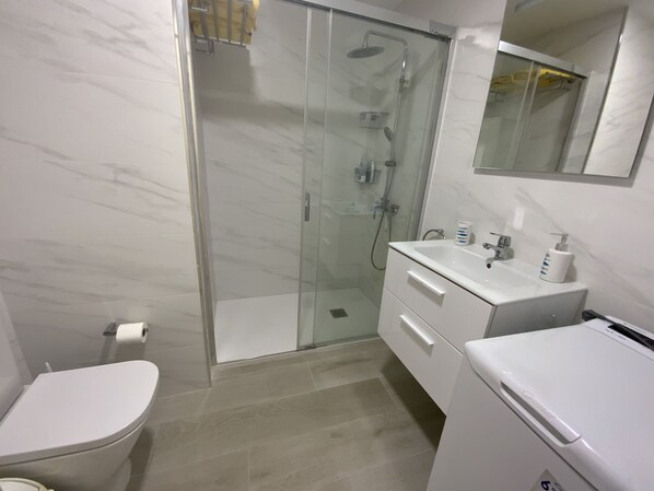 Ein modernes Badezimmer mit einer Duschkabine, einer Toilette, einem Waschbecken mit Spiegel und einem Schrank.