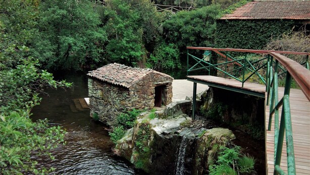 A rustic stone building with a tiled roof, a wooden bridge, and a small waterfall. - Casas da Encosta, Shale Houses, Accommodation in Shale Village - Free Wifi (Sobreira Formosa)