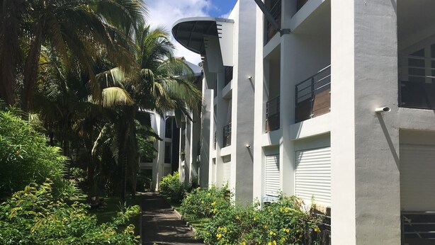 A pathway flanked by lush greenery and white buildings with balconies. - Charming T2 in Boucan Canot - La Canotière du Boucan - 55 m² (Boucan Canot)