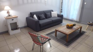 A modern living room with a grey sofa, a wooden coffee table with fruit, a patterned chair, and a small white side table with a lamp. - Charming T2 in Boucan Canot - La Canotière du Boucan - 55 m² (Boucan Canot)