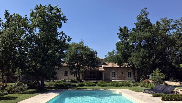 A swimming pool with a wooden deck, surrounded by lush greenery and a stone building. - Beautiful Provence House in the Luberon - Heated Swimming Pool & Large Gardens. (Roussillon)