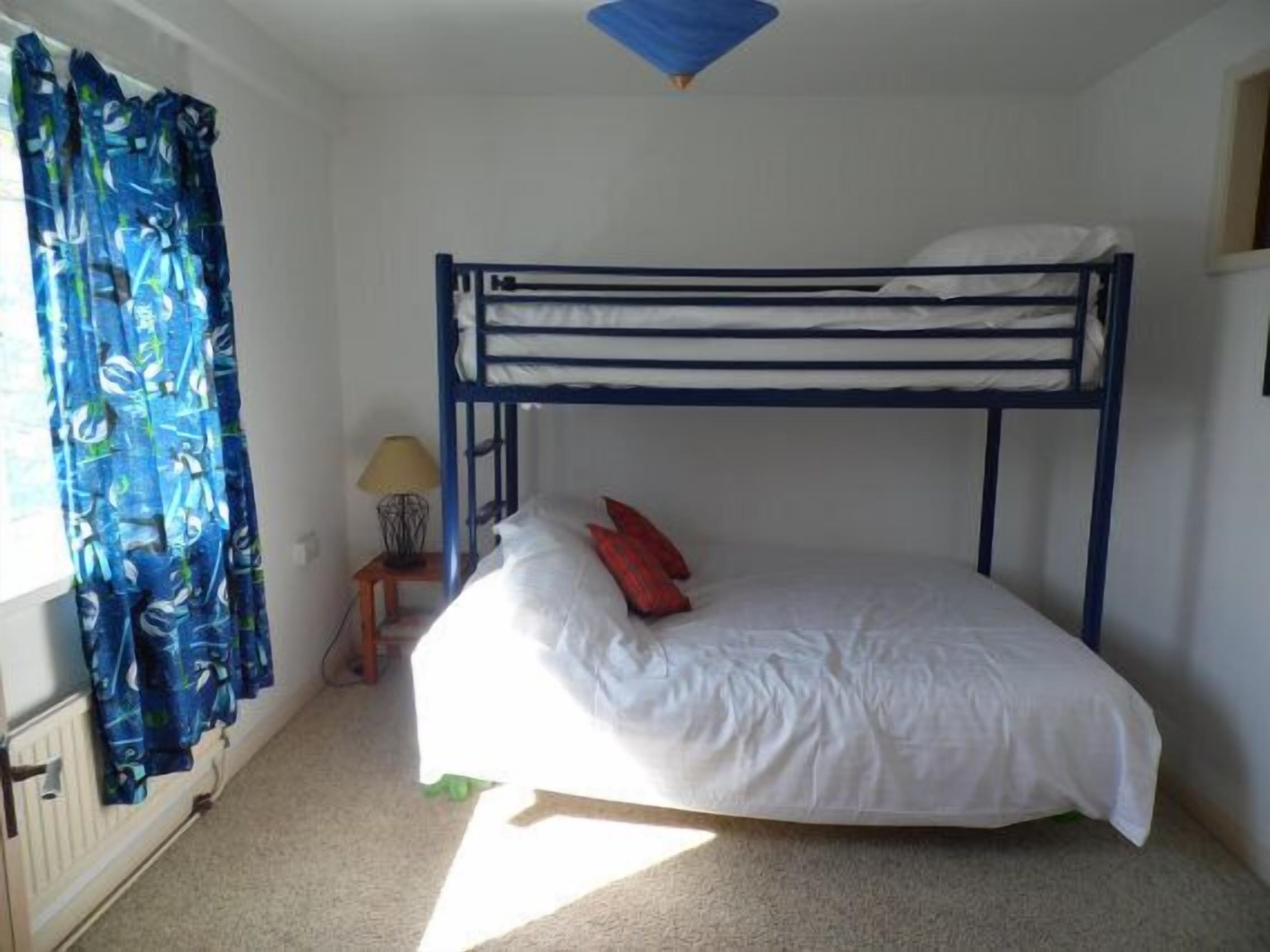 Une chambre avec un lit superposé, une fenêtre, des rideaux, une lampe et un radiateur.