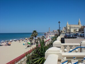 A beach with palm trees, a lighthouse, and a historic building. - Caracola Apartment. Air conditioning, Wifi, Terrace, Garage. Beach 300 meters (Chipiona)