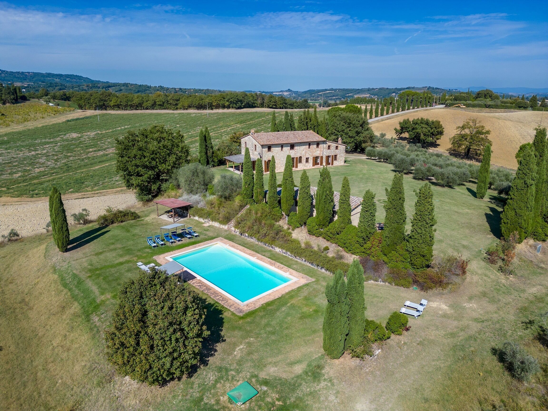 Une vaste villa en pierre dotée d’une piscine, entourée de jardins bien entretenus et de grands cyprès.