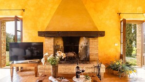 A cozy living room with a fireplace, a television, and a dining area with flowers and a bottle of wine. - Il Poderuccio 17, Emma Villas (Cetona (Siena))