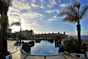 Ein Pool mit Meerblick, umgeben von Palmen und einem Gebäude mit einem Ziegeldach.