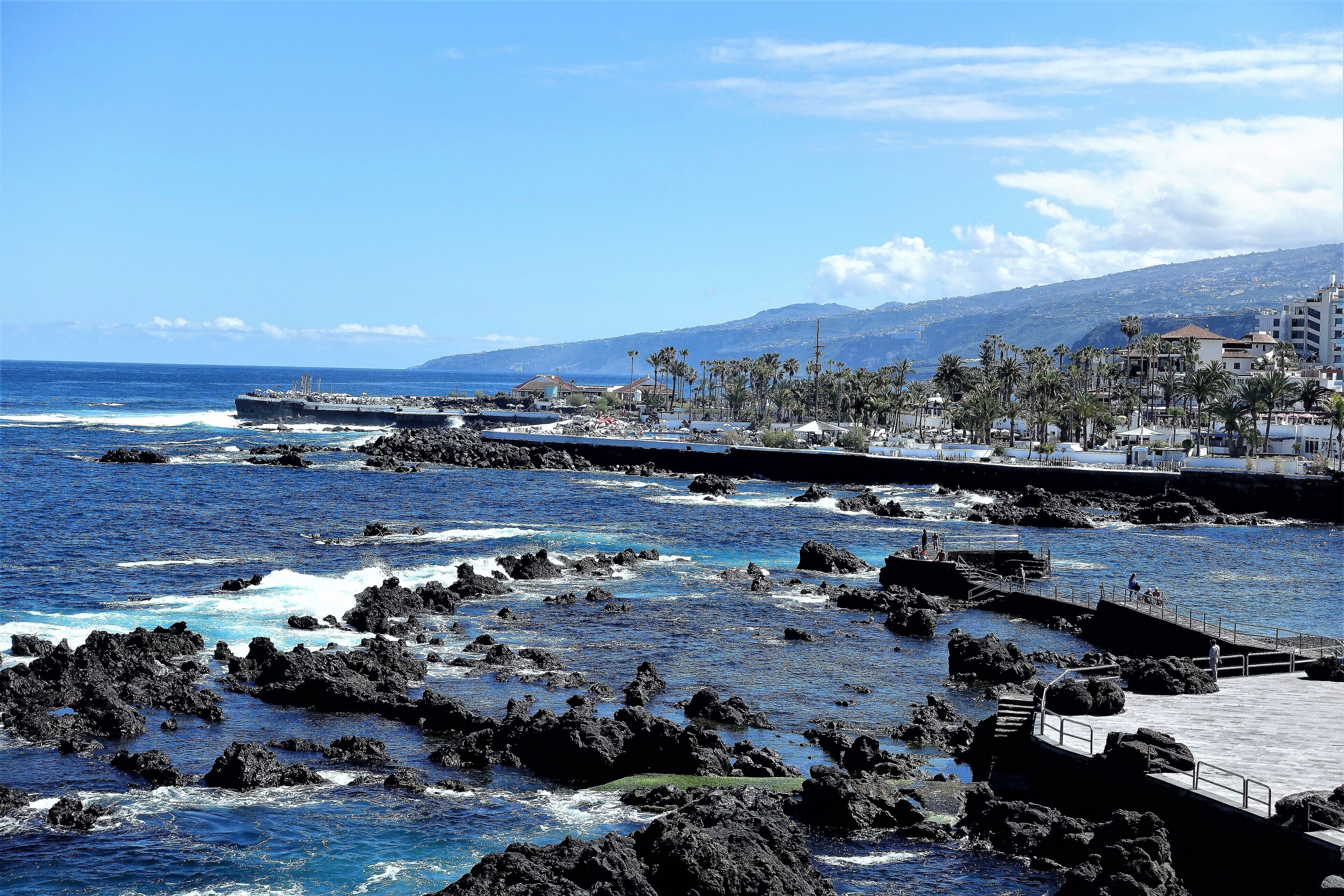 A coastal area with rocky waters, a pier, and buildings in the background.