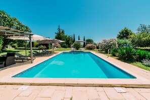 Una piscina rectangular con solárium empedrado, rodeada de sillones de playa y sombrillas.