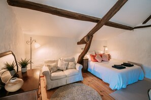 Un dormitorio acogedor con techo de madera, un sofá, una cama con colcha azul y una mesita con lámpara.