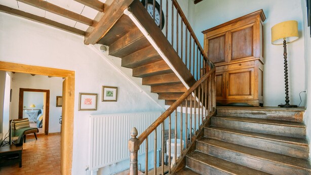 Un escalier en bois avec un radiateur blanc en dessous, une armoire en bois sur la droite et une lampe posée sur le sol.