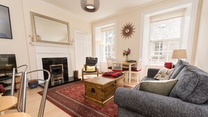 A living room with a fireplace, a sofa, a coffee table, and a wooden chest. - Luxury Thistle New Town 1 Bed Apt Super King (Edinburgh)