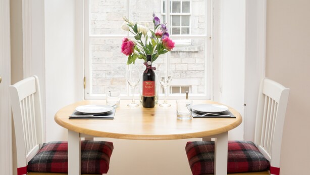 A dining table with a bottle of wine, glasses, and plates set for two. - Luxury Thistle New Town 1 Bed Apt Super King (Edinburgh)