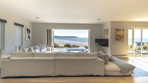 Ein modernes Wohnzimmer mit einer großen Couch, einem Fernseher und Blick auf den Strand.