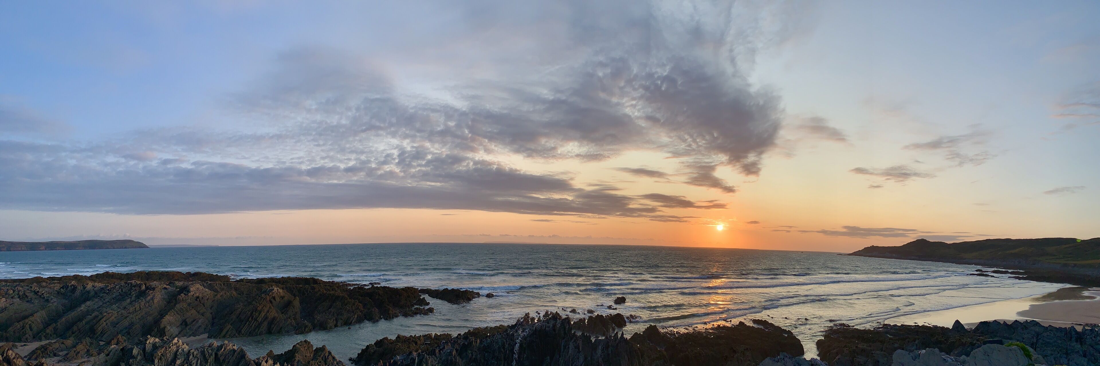 Kystlandskab med klippefyldt terræn og en solnedgang over havet.