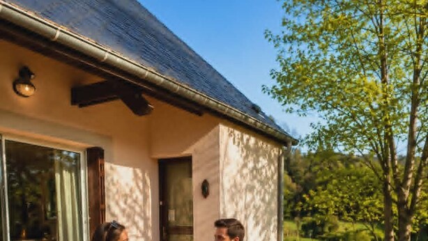 Un couple est assis sur une terrasse en bois, avec une maison en arrière-plan.