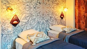 Une chambre avec deux lits, un papier peint à motifs et des lampes fixées au mur.