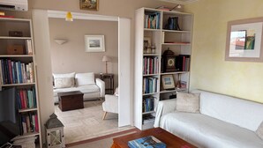 Una sala de estar con un sofá blanco, una mesa de centro de madera, una estantería y una lámpara.