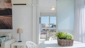 A modern living room with a white sofa, a small table, and a round table with a plant. There is a view of the city through large windows. - COZY AND SPACIOUS APARTMENT - WELL LOCATED AND DIRECT SEA VIEW (Torremolinos)