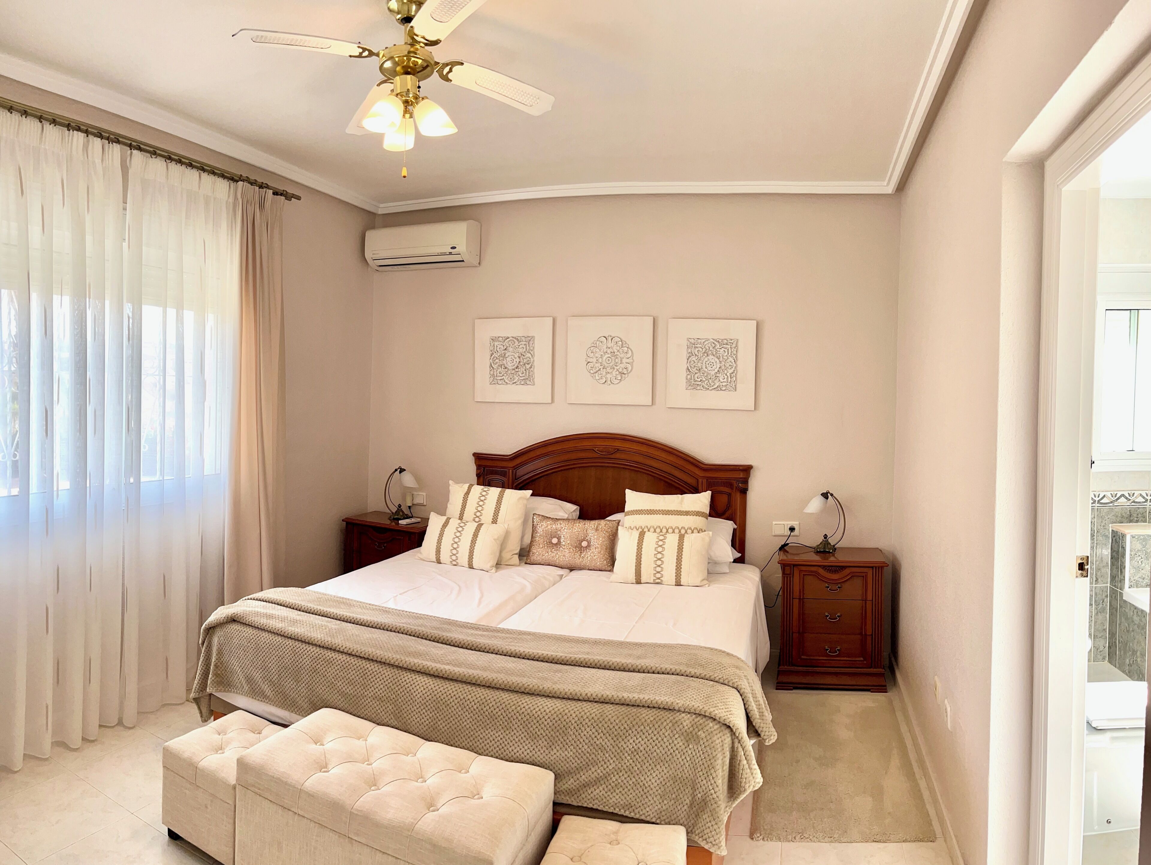 A bedroom with a large bed, two bedside tables, a ceiling fan, and a window with sheer curtains.