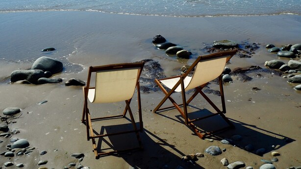 Deux chaises pliantes vides sur une plage rocheuse, avec l’océan en arrière-plan.