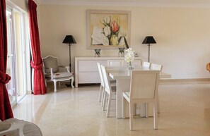 A dining area with a white table and chairs, a painting above the table, and two lamps on either side.