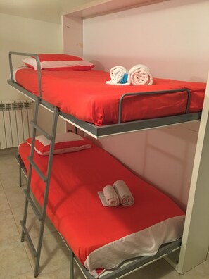 A bunk bed with red bedding and two rolled towels on the top bunk.