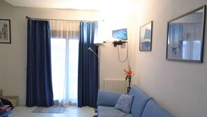 A living room with a blue sofa, a radiator, a TV, and a window with curtains. - VILLETTA TO FORMATION WITH GARDEN 300MT FROM THE SEA (Pittulongu)