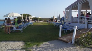 A beachside area with lounge chairs and umbrellas, a covered seating area, and a view of the sea. - VILLETTA TO FORMATION WITH GARDEN 300MT FROM THE SEA (Pittulongu)