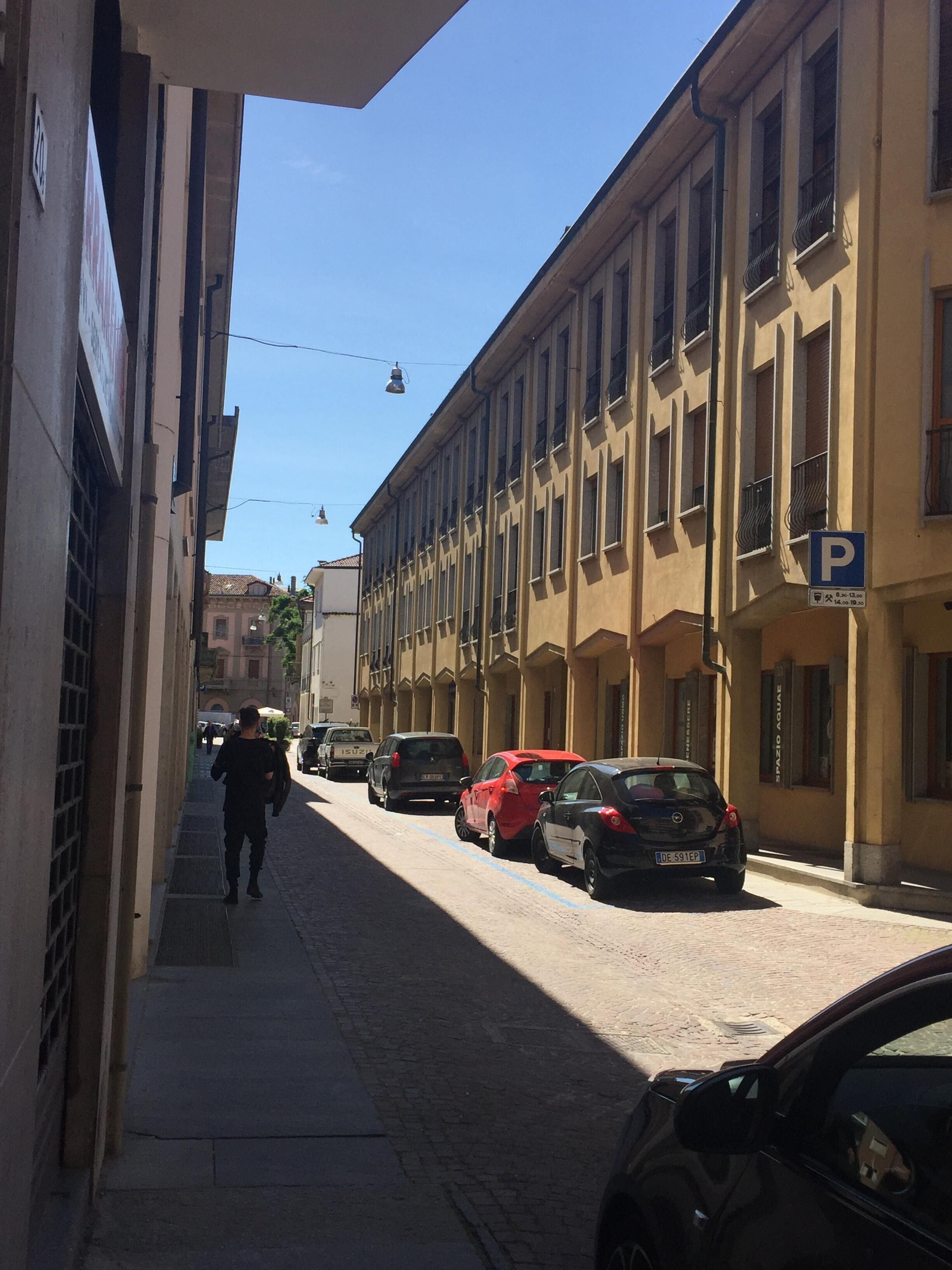 Une rue étroite bordée de voitures garées et d’immeubles dotés de balcons.