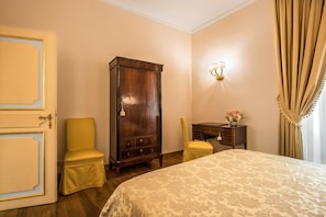 A hotel room with a bed, a wooden wardrobe, a desk with a lamp, and a chair.