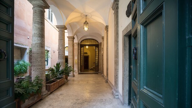 A corridor with columns, a green door, and potted plants.