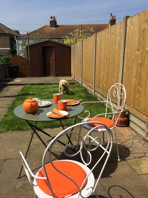 A backyard with a small table and two chairs, a dog, and a wooden fence.