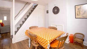 A dining area with a polka dot tablecloth, wooden chairs, a chandelier, a clock, and a framed map on the wall. - Goodwin Sands Cottage - 50 meters from the beach  (Deal)