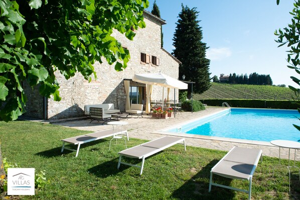 Une villa avec une façade en pierre, une piscine et un espace salon extérieur.