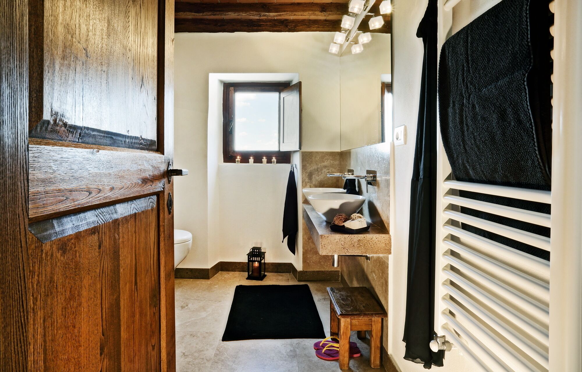 Ein Badezimmer mit Holztür, Fenster, Waschbecken und Heizkörper.