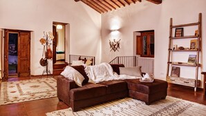 A cozy living room with a brown sofa, patterned rugs, wooden beams, and a bookshelf. - Secluded villa between Chianti vineyards, private pool, tennis, large garden (Gaiole In Chianti)