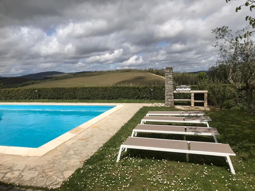 A swimming pool with lounge chairs and a stone structure, surrounded by a hedge and a view of rolling hills.