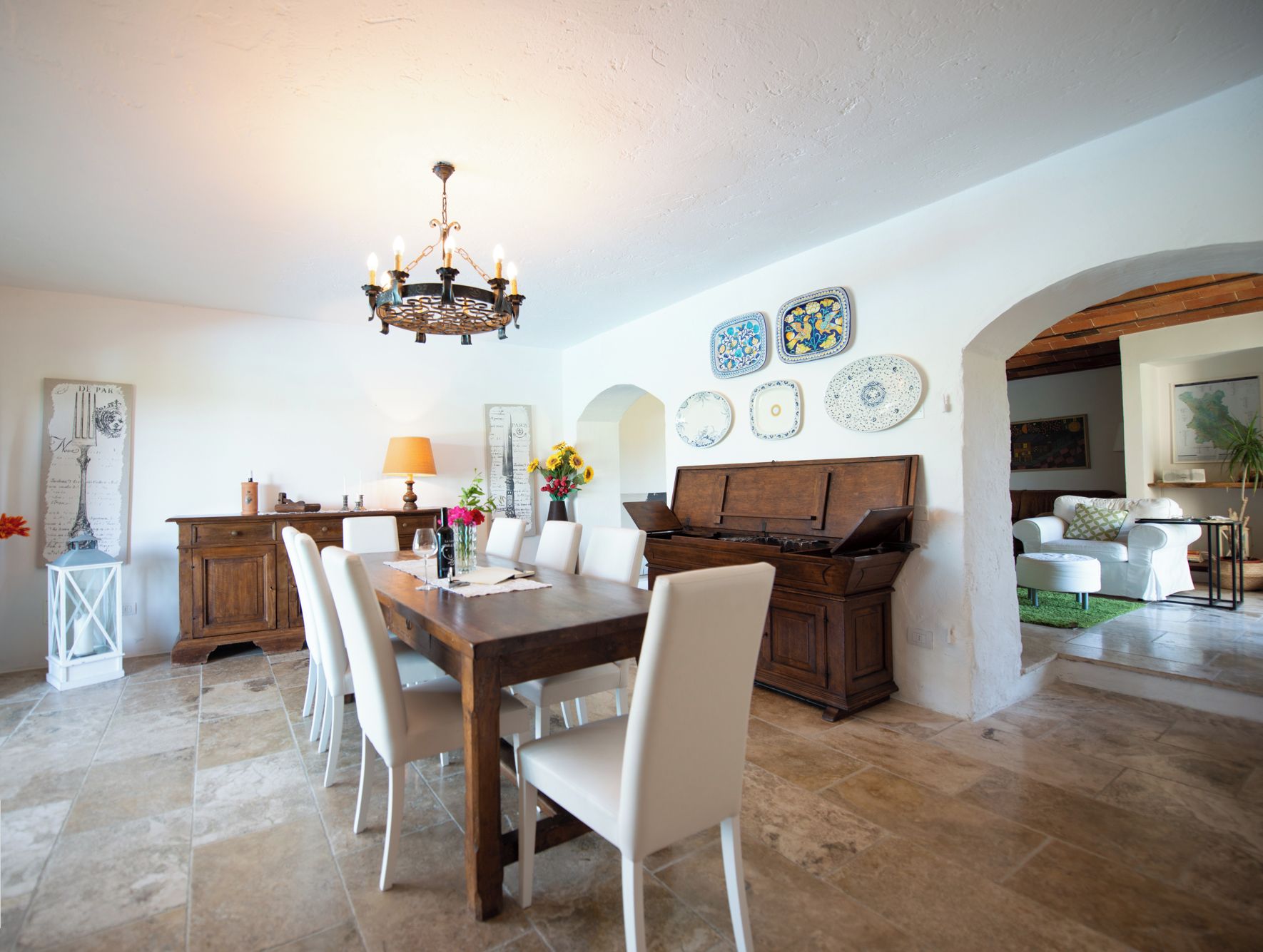 A dining area with a wooden table, white chairs, a chandelier, and a piano.