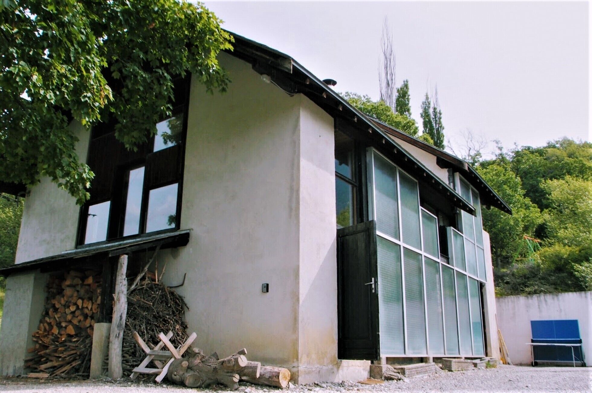 A building with a large windowed section, a door, and a pile of firewood outside.