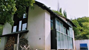 A building with a large windowed section, a door, and a pile of firewood outside.