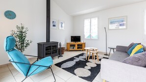 Moderni olohuone, jossa on sohva, nojatuoli, televisio, takka ja suuri ikkuna.