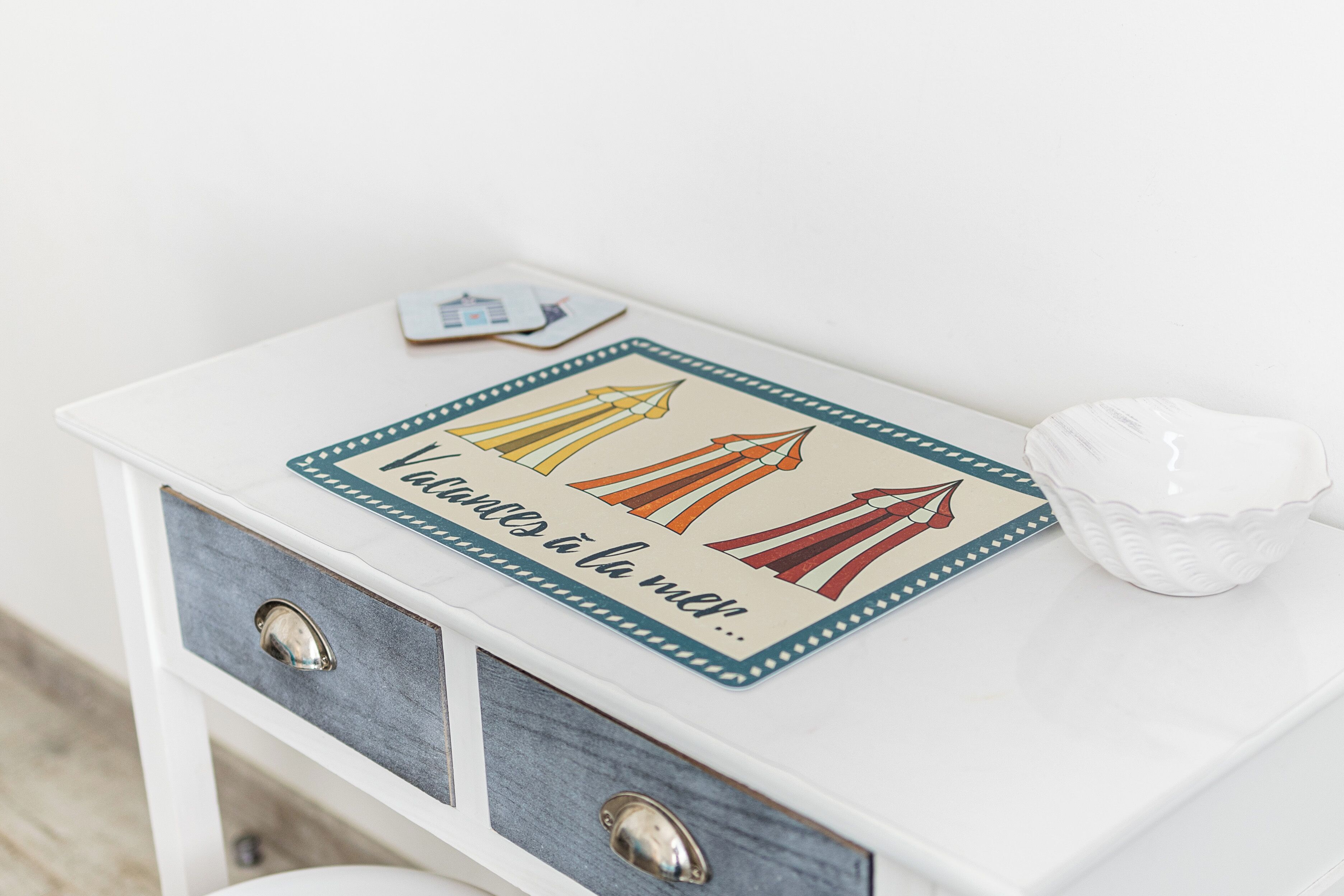 A white bedside table with a decorative sign featuring a pencil and a red airplane, and a small white bowl.