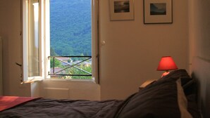 A bedroom with a bed, a window with a view of a forest, and two framed pictures on the wall. - Stunning views - Beautiful holiday home in a friendly Italian village  (Dumenza (VA))