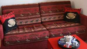 A red sofa with patterned cushions and two pillows with 'MOCHA' text. A tray with a teapot, cups, and saucers is on the table in front. - Stunning views - Beautiful holiday home in a friendly Italian village  (Dumenza (VA))