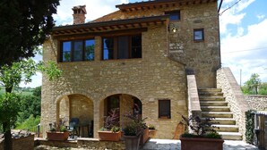 A stone house with a staircase leading to a second floor, outdoor seating area, and potted plants.